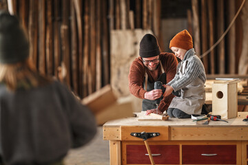 Little boy with father assembling wooden bird house in workshop