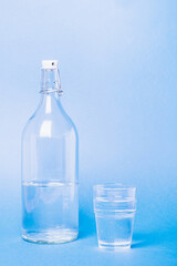 Glass with water near to bottle on blue background