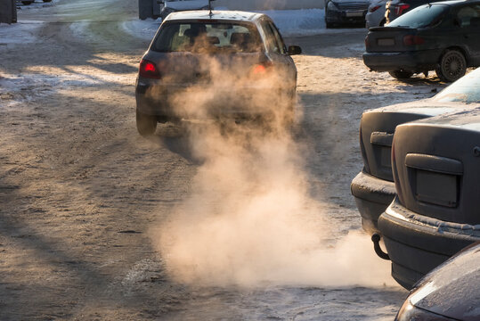 Car smog and air pollution from the exhaust pipe in the city in the winter. Smoke in the rays of the sunset. The concept of the need to switch from internal combustion engines to electric vehicles. © sergeimelnikov