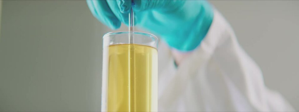 Man measuring properties of yellow liquid in graduated cylinder by hydrometer. Working in factory laboratory concept.