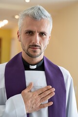 Catholic priest cleric praying with his hand on heart