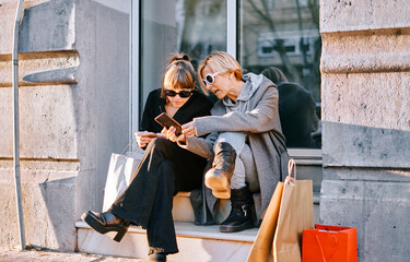 Two girlfriends are sitting in a portal with shopping bags