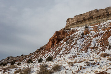 Fototapeta na wymiar Snow covered red rock mountain with mesa plateau and brush with overcast sky in rural New Mexico