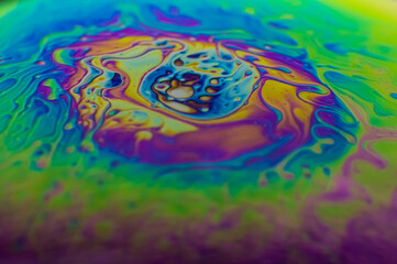 Side of a soap bubble macro, close up detailed shot. Bright, rainbow colors looking like a imitation of space, planet on black background. 