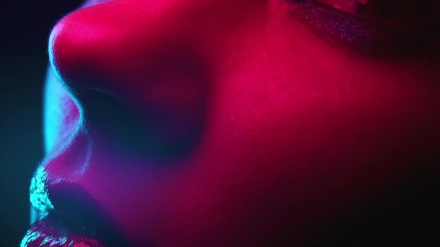 Female face extremely close-up. Woman with amazing shining evening makeup under colorful neon light. Beauty, body part, cosmetics concept.