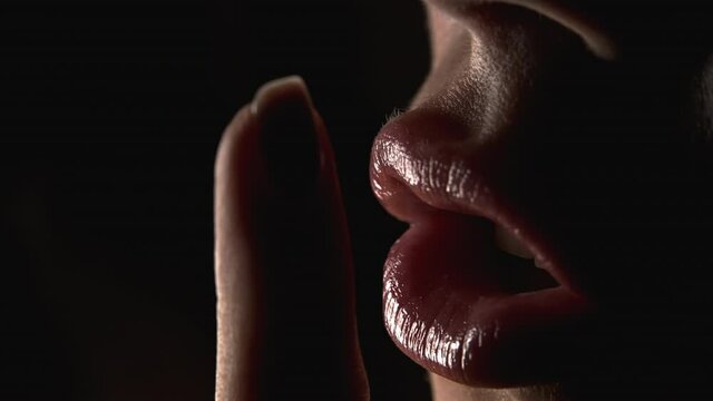 Gesture of shhh, secret, silence. Close-up view of woman face, she holding finger on her lips over black background.