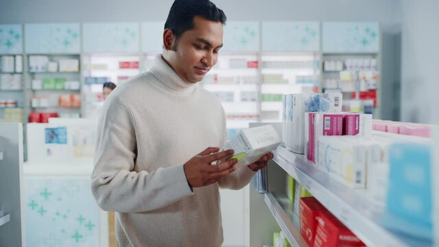 Pharmacy Drugstore: Portrait of Handsome Indian Man Choosing to Buy Medicine Browsing through the Shelf, Successfully finds what he Needs, Smiles Happily. Modern Pharma Store Health Care Products