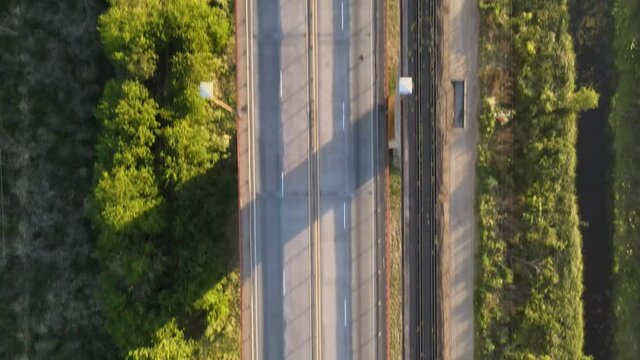 Aerial top down dolly in following a road and railway cable-stayed bridge surrounded by vegetation at golden hour