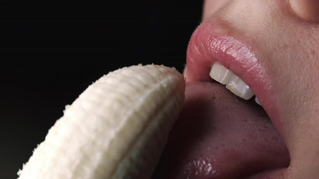 Sexy young woman seductively licking fresh banana. Macro view of lady facial expression of desire. Close-up of female mouth, sensual footage. Slow motion.