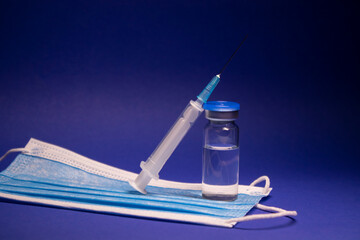 Vaccine bottle phial with no label on blue medical mask and medical syringe with injection needle....