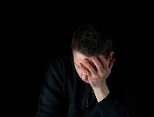 Depressed mature man holding his face in the dark while showing emotion of sadness