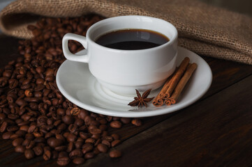 A cup of coffee, roasted coffee beans, cinnamon sticks and star anise on a wooden table.