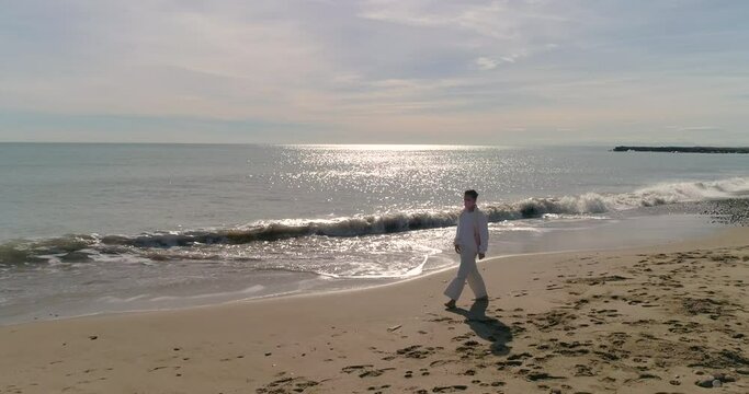 Mujer madura con mascarilla protecci&oacute;n coronavirus paseando de blanco por la playa