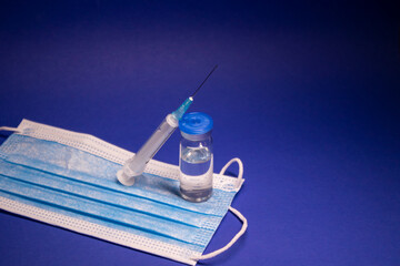 Vaccine bottle phial with no label on blue medical mask and medical syringe with injection needle....