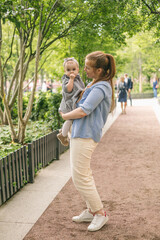 A young mother walks with a one-year-old baby, holds him in her arms, hugs. Communication with the child for his harmonious development