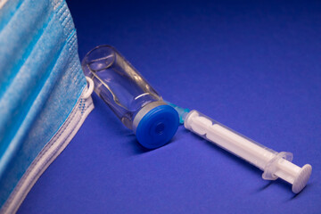 Vaccine bottle phial with no label near blue medical mask and medical syringe with injection...