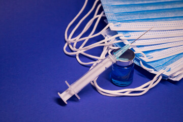 Vaccine bottle phial with no label and medical syringe with injection needle near pile of blue medical masks . isolated on blue background. cure. Development of coronavirus vaccine COVID-19