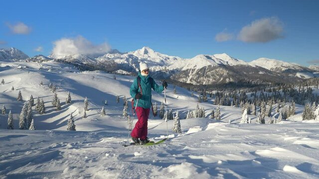 COPY SPACE: Young Caucasian woman on a ski touring trip to Slovenia hikes up a snow covered hill overlooking the picturesque untouched valley. Fit female tourist splitboarding in Velika Planina.
