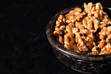 Carved wooden bowl with peeled walnut seeds on a black background.