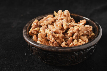 Carved wooden bowl with peeled walnut seeds on a black background.