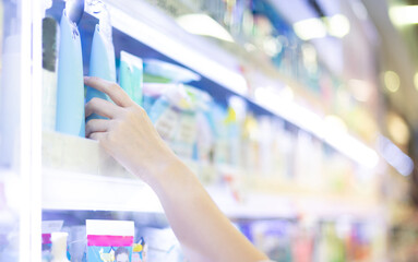 Female  hands holding body lotion on the shelf of cosmetic at the department store,