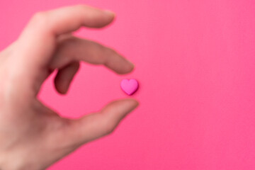 The hand takes a pink heart isolated in the center on an empty colorful pink background. Symbol of love for Happy Women's, Mother's, Valentine's Day, Birthday greeting romantic postcard. Flat lay, top