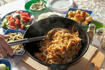 Seafood pilaf in an old cast iron cauldron. table with vegetable dishes