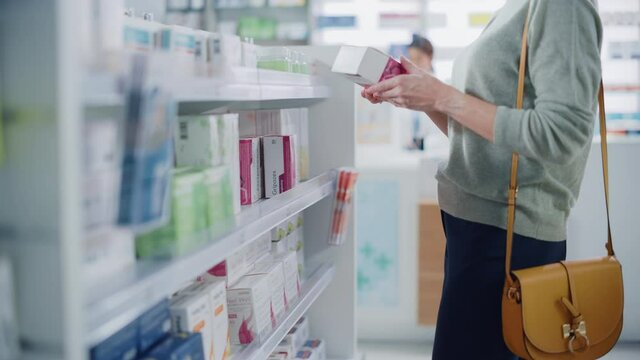 Pharmacy Drugstore: Anonymous Woman Chooses and Picks the Best Medicine Package, Supplemen Box, Drugs, Pills of the Shelf and Goes to Cashier Counter. Modern Pharma Store Health Care Products