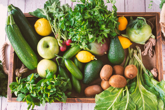 Healthy Greens And Fruits Viewed From Above In A Vegetable Box. Chard, Mango, Avocado, Lemon, Kiwi, Green Apple, Kohlrabi, Marrows, Cucumber, Parsley, Mint.