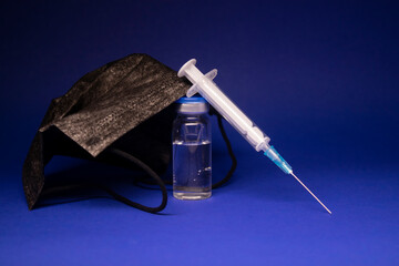 Vaccine bottle phial with no label near black medical mask and medical syringe with injection...