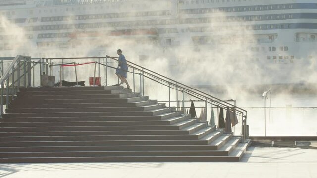 Telephoto shot of silhouetted single person walking up steps away from steaming outdoor pool with huge cruise ship in the background