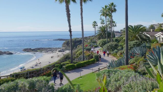 People walking along a path, overlooking a beach and Ocean, in Laguna Beach California. Slowed to half speed.