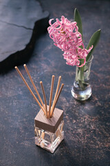 Moody dark background with aroma reed diffuser and pink hyacinth flower in glass on aged textured...