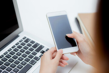 Hand of young woman working with laptop computer and smartphone mockup on desk at home, notebook and phone display blank screen, freelance look message to internet, business and communication concept.