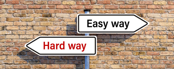 signpost with two arrow-shaped signs with the words HARD WAY and EASY WAY in opposite direction in front of a brick wall