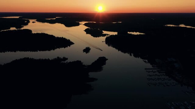 Aerial silhouette view of a boat arriving at a marina, sunset, in Scandinavia - reverse, drone shot