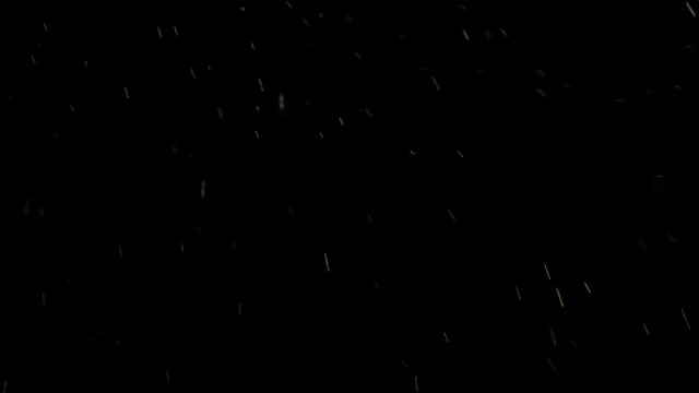 Shiny raindrops falling against dark black night background as moving particles.