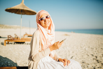 Smiling muslim woman with a headscarf hijab using her smartphone outdoors. Technology and religion concept. Young islamic female culture.Modern middle eastern arab woman. Muslim business woman