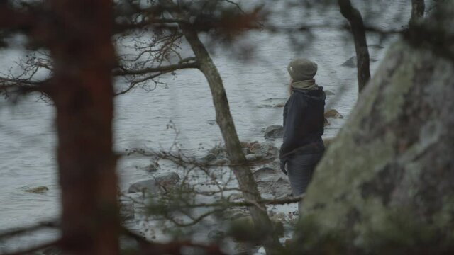 Lone girl in winter clothes standing looking out over lake in winter