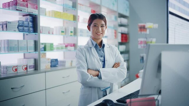 Pharmacy Drugstore: Beautiful Asian Pharmacist Uses Checkout Counter Computer, Does Inventory Checkup, Online Prescription of Medicine, Pills, Supplements Looks at Camera Smiling. 