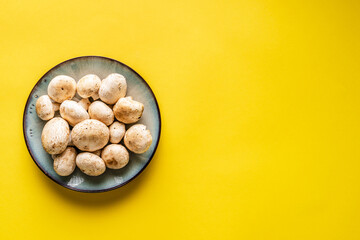 Top view on plate with white common champignon mushrooms on yellow background