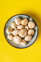 Fototapeta premium Top view on plate with white common champignon mushrooms on yellow background