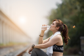 woman in sportswear drinking water from bottle after exercise sitting outdoor on train railway. Athlete drinking water is beneficial and refreshing to the body.