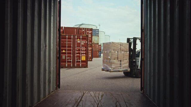Forklift Driver Unloading a Shipping Cargo Container with a Full Pallet with Carboard Boxes in Logistics Operations Port Terminal. Camera View from Inside Shows How Pallet is Lifted and Taken Away.