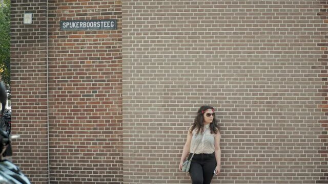 Stylish Woman with Sunglasses Leaning and Posing in front of Classical Red Brick Stone Wall in Cozy Town in Netherlands in slowmo