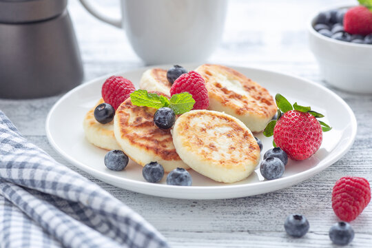 Cottage cheese pancakes with fresh berries on white wooden table. Tasty breakfast food. Syrniki - Image