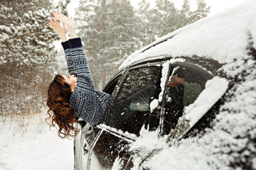 Young attractive woman travelling in car on winter road and snow covered forest.