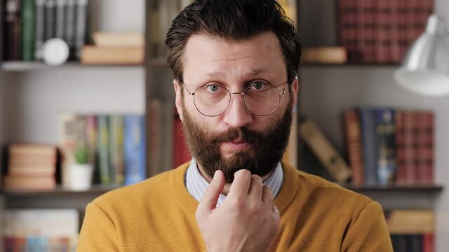 Man is embarrassed, shy. Slightly confused bearded man in glasses in office or apartment room shyly looks away from camera, looks embarrassed. Close-up and slow motion