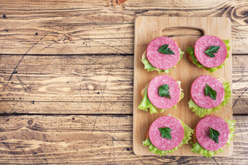 Obraz na płótnie Canvas Sandwiches with lettuce leaves and sliced salami sausage on a wooden Board. top view copy space