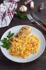 Delicious Asian pilaf, stewed rice with vegetables and chicken drumstick on a plate. Wooden rustic background.